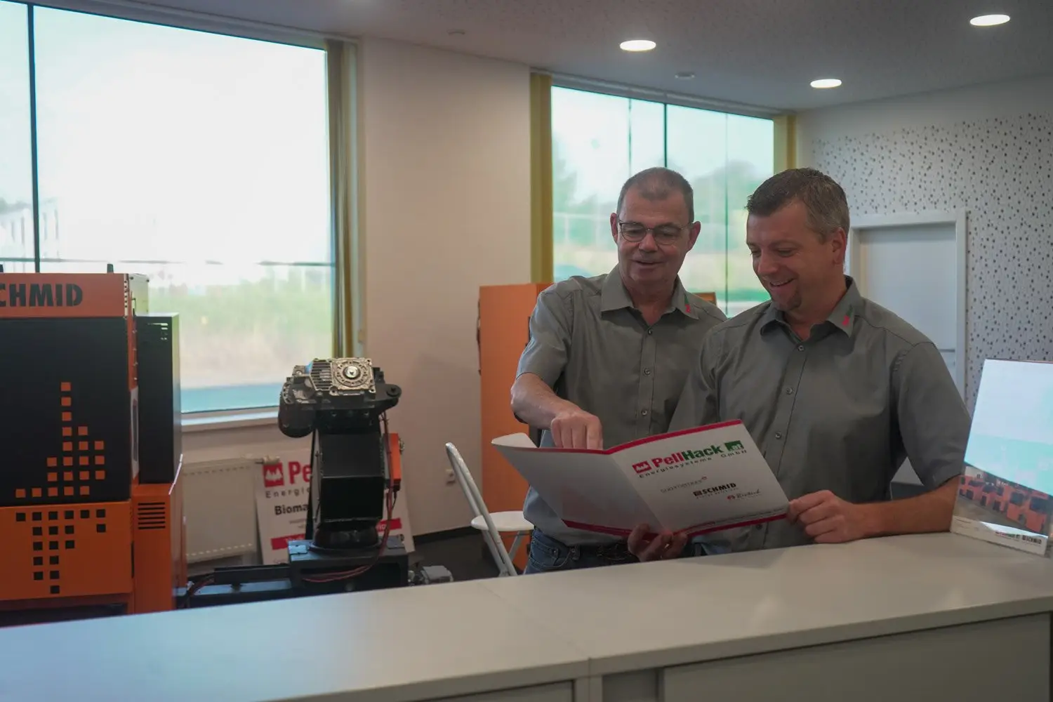 Zwei Mitarbeiter der Firma Pellhack lesen eine Broschüre und dahinter ist der Schauraum mit Pelletsheizungen der Firma Schmid Energy Solutions